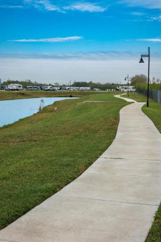 A concrete walking path stretches away in the distance alongside a shallow fishing pond at the Medical Center RV Resort in Houston, Texas. 